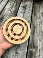 The hand of a person is shown holding a round wood trivet with circles cut out of it.