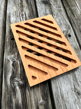 The back of a rectangular wood trivet with diagonal lines cut out of it sits on a gray picnic table a grey wood table..