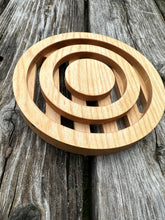 A round wood trivet with circles cut out of it, sitting on a weathered picnic table. 