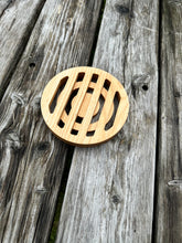 The back of a round wood trivet sitting on a grey wood table.