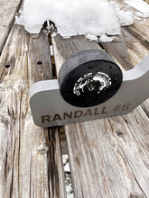 Close-up of hockey stick blade engraved with a player's name and number, stick sits on weathered wood table with a small pile of snow in the background.