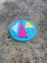 Round cribbage board on concrete table with 90s retro style graphics in bright colors with metal pegs